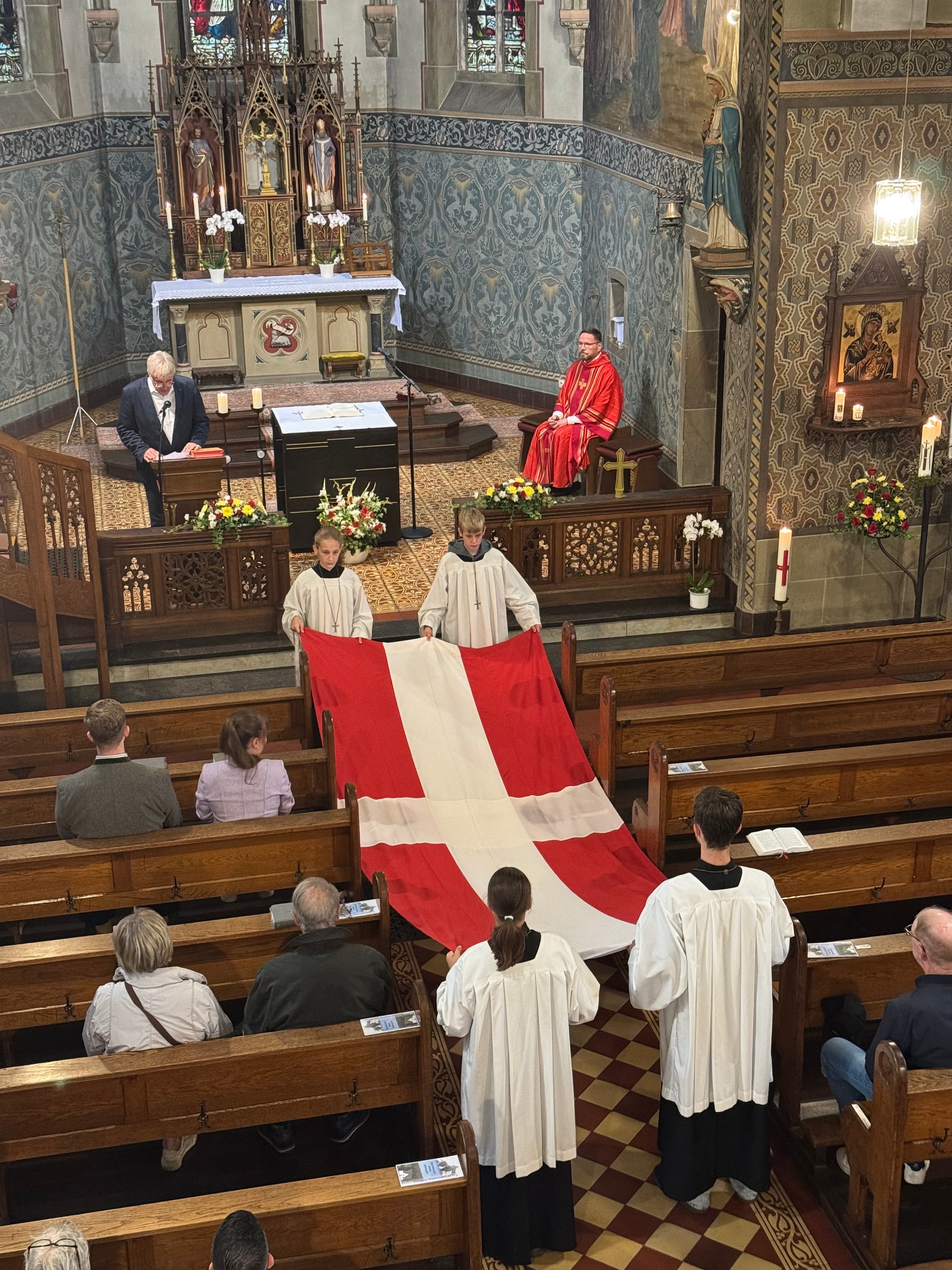 Messdiener tragen die rote Flagge mit weißem Kreuz zum Altar