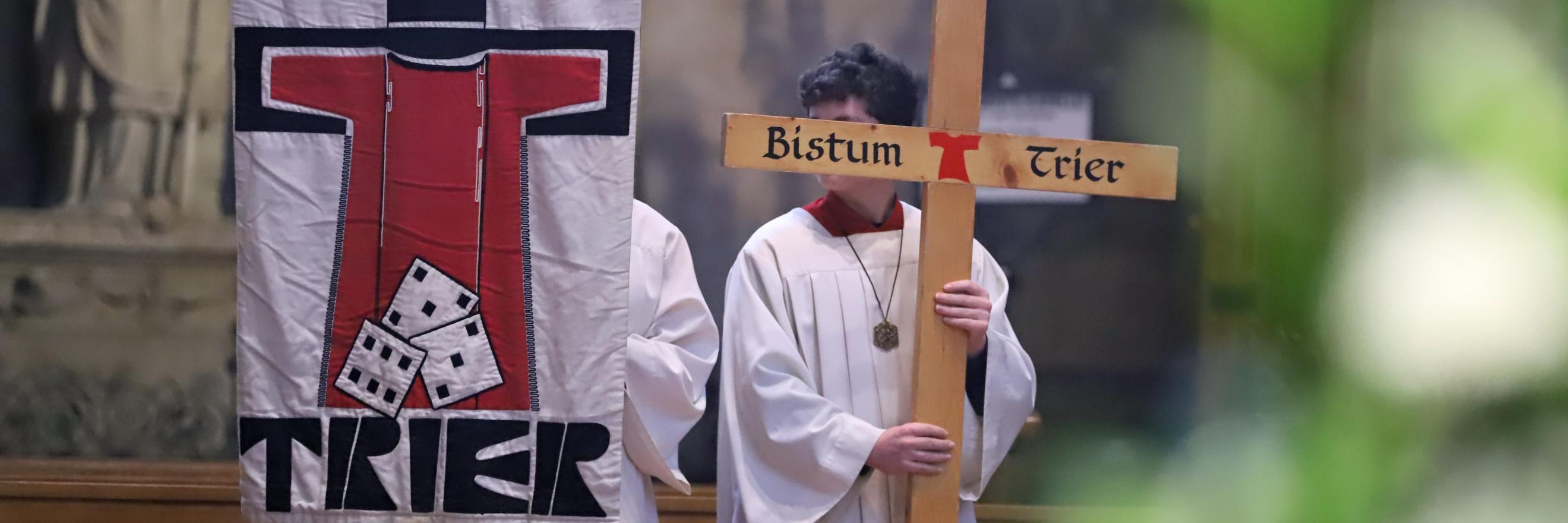 Zwei Messdiener in einer Messe; einer hält die Pilgerfahne mit der Aufschrift 'Trier' hoch, der andere ein Kreuz, auf dem Bistum Trier steht. (c) Bistum Trier/Inge Hülpes Zwei Messdiener in einer Messe; einer hält die Pilgerfahne mit der Aufschrift 'Trier' hoch, der andere ein Kreuz, auf dem Bistum Trier steht.